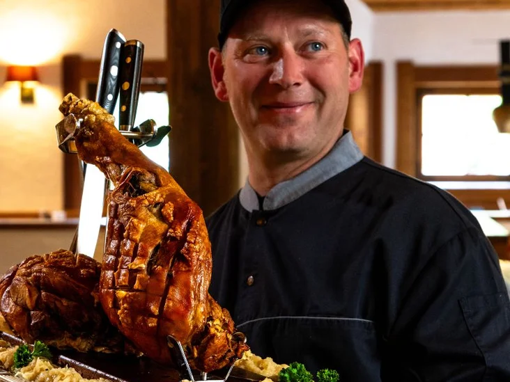 Koch einer Bavaria Alm präsentiert eine Haxe