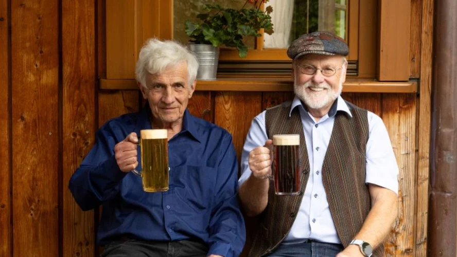 Gäste auf der Terrasse einer Bavaria Alm mit einem gezapften Bier