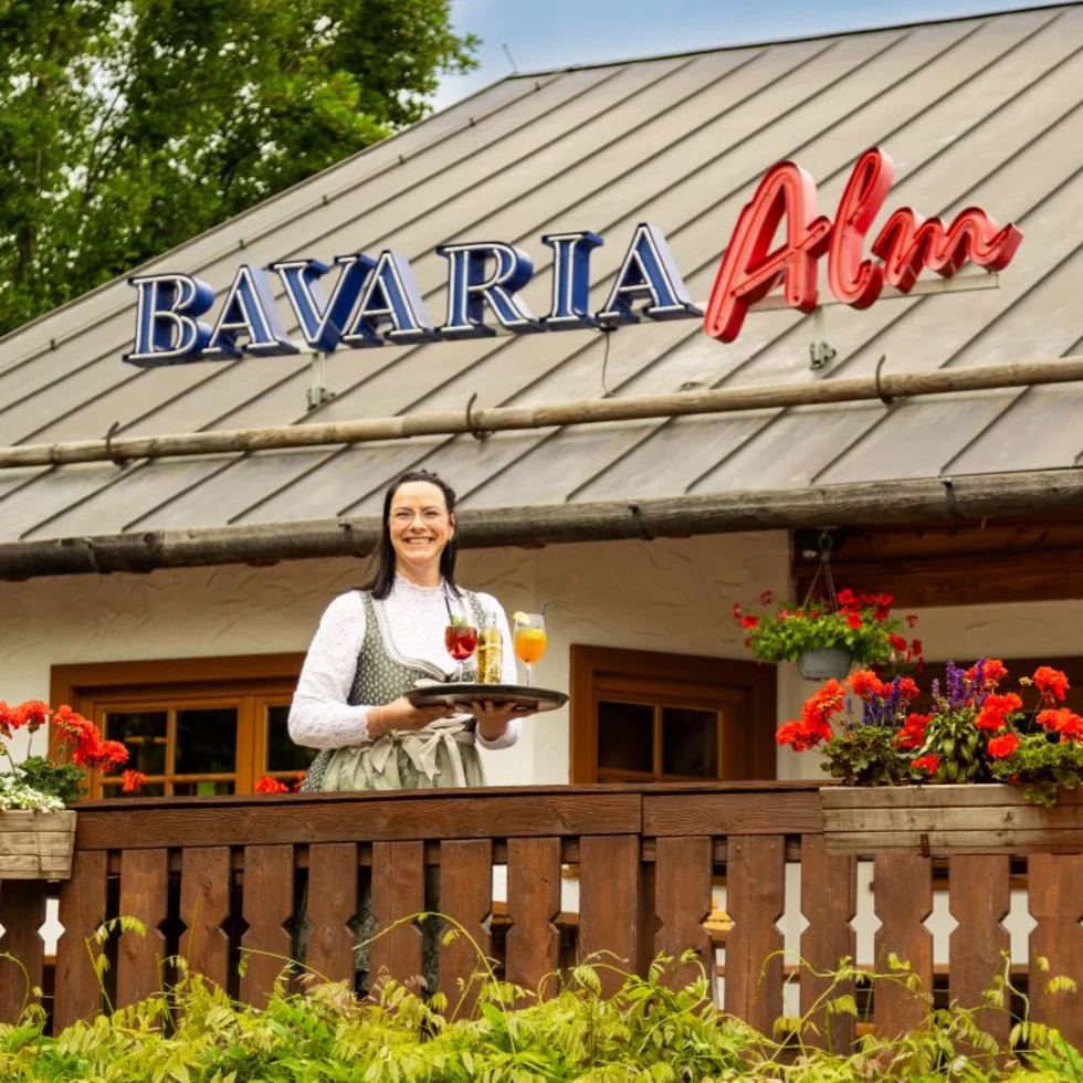 Außenansicht einer Bavaria Alm mit einer Mitarbeiterin