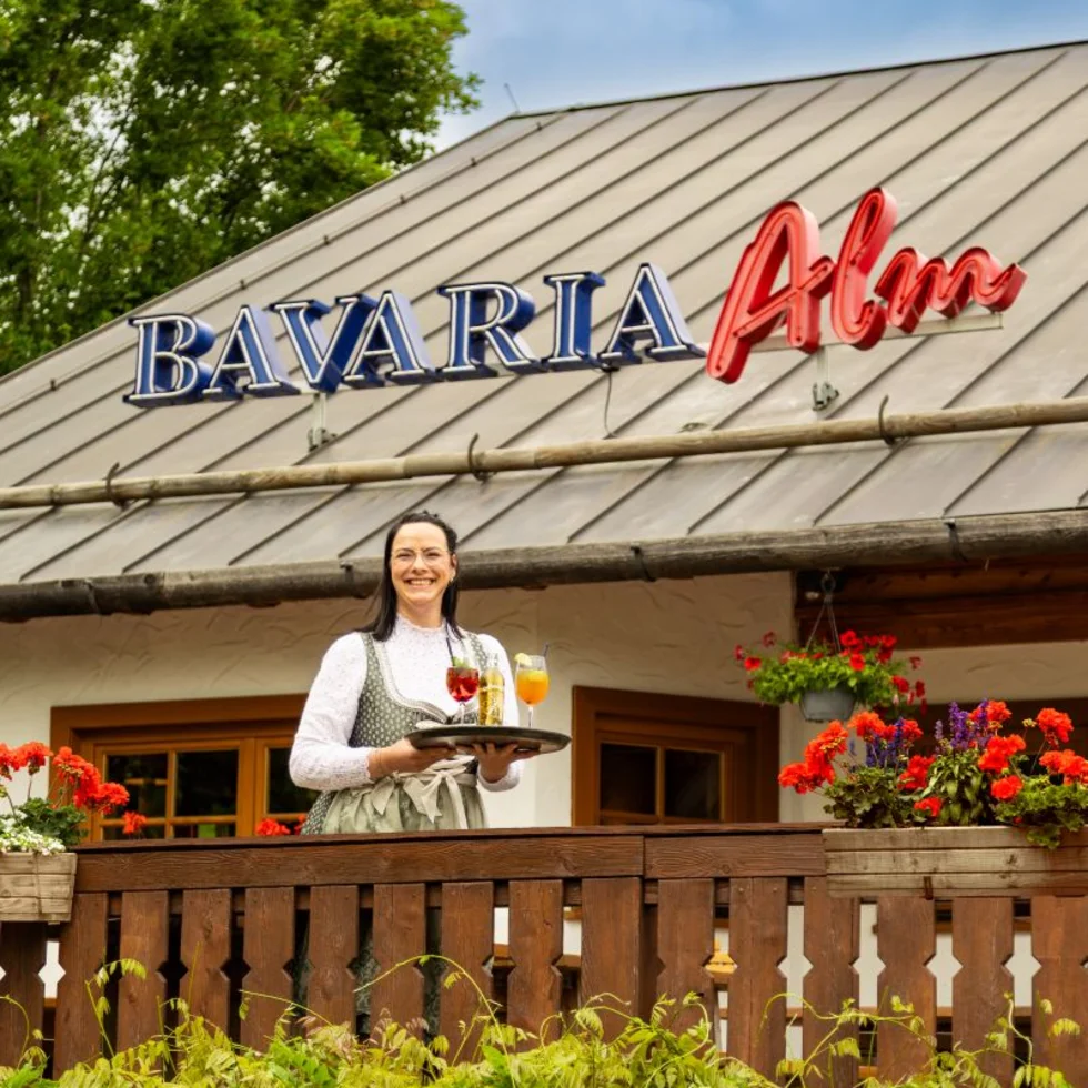 Außenansicht einer Bavaria Alm mit einer Mitarbeiterin