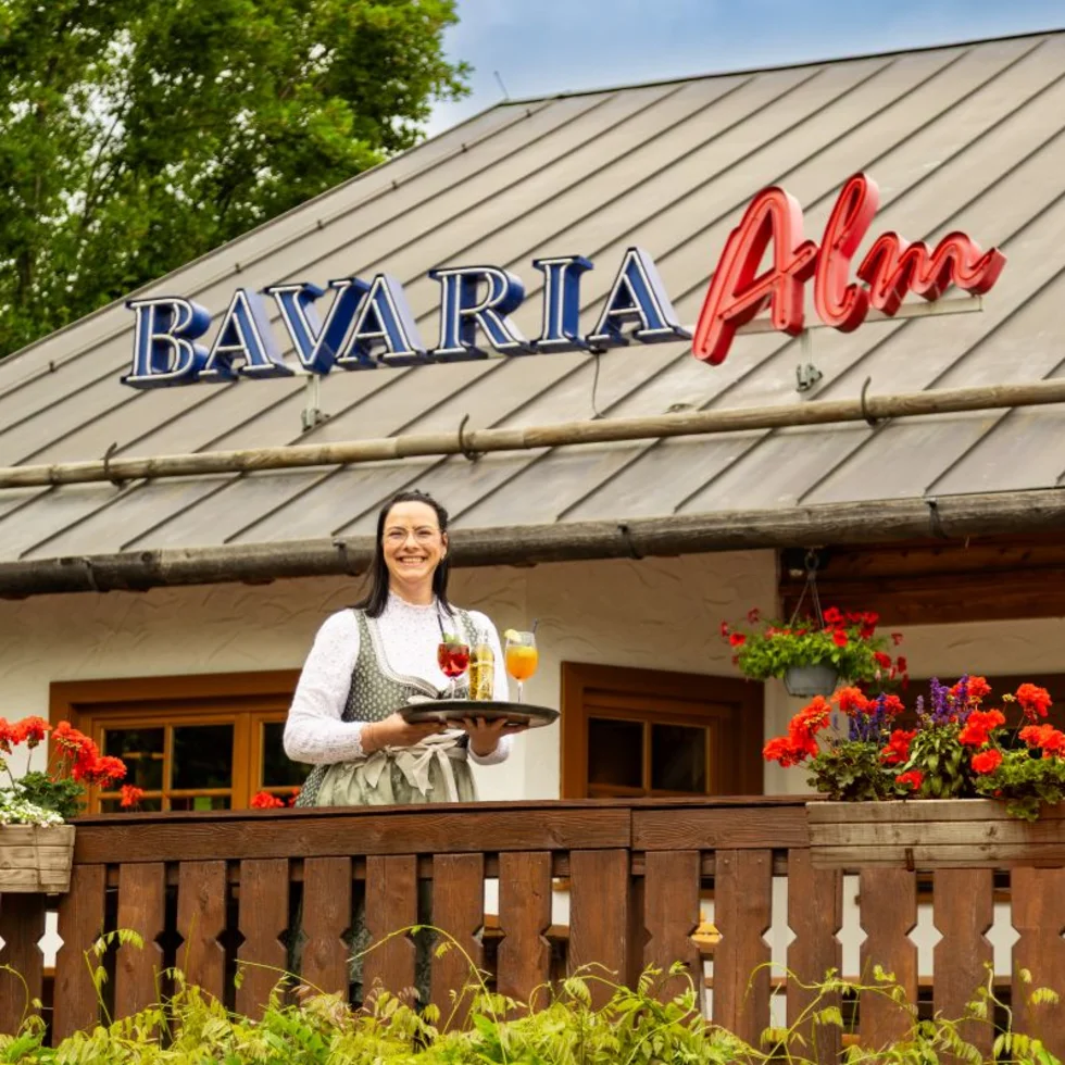 Außenansicht einer Bavaria Alm mit einer Mitarbeiterin