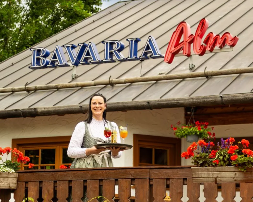 Außenansicht einer Bavaria Alm mit einer Mitarbeiterin