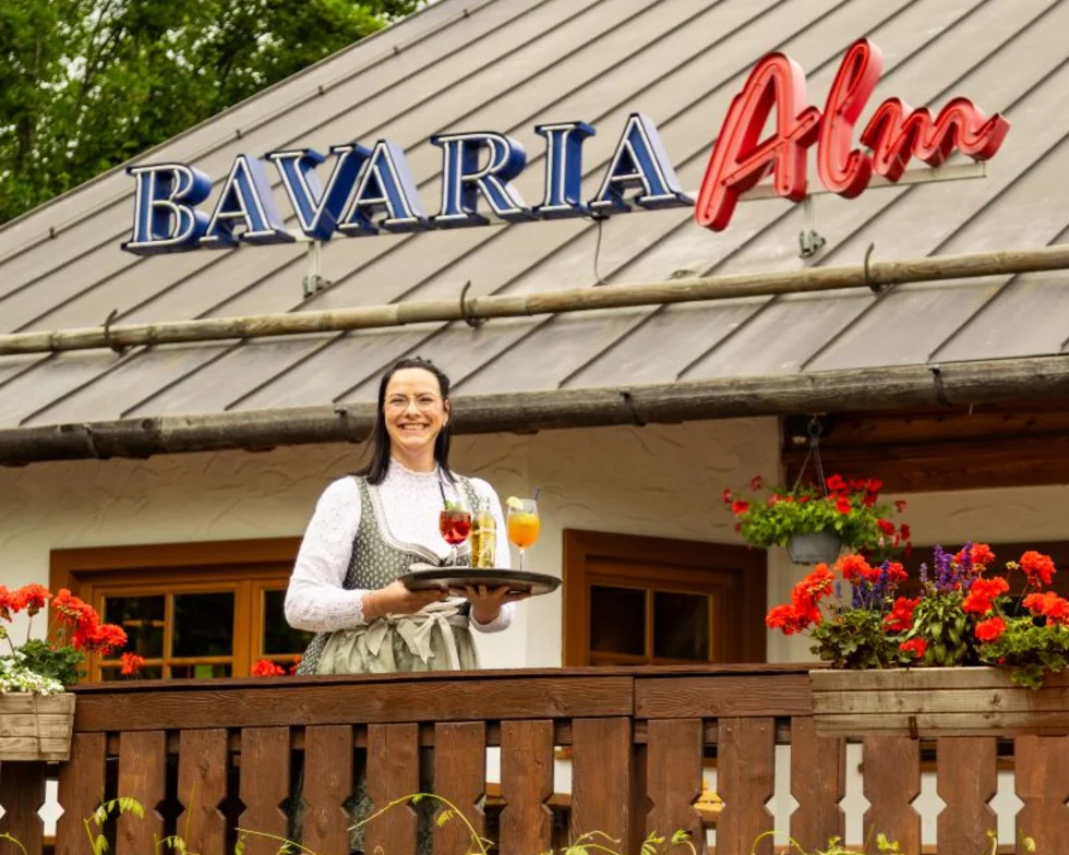Außenansicht einer Bavaria Alm mit einer Mitarbeiterin